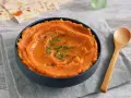 Un tazón de cremoso puré de boniato, adornado con aceite y hierbas, junto a una cuchara de madera.