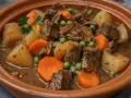 Un reconfortante plato de carne guisada con patatas, zanahorias y guisantes en una cazuela de barro.