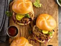 Dos sándwiches de pulled pork jugoso, con repollo morado, pepinillos y salsa barbacoa en un plato de madera.
