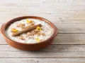Un tazón de arroz con leche cremoso, espolvoreado con canela y adornado con cáscara de naranja y una rama de canela.