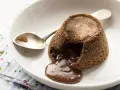 Coulant de chocolate recién hecho, con su interior líquido y cremoso desbordándose. Una cuchara plateada espera pacientemente.