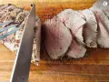 Un cuchillo corta un jugoso roast beef en rodajas sobre una tabla de madera.