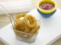 Crujientes aros de cebolla dorados en una cesta metálica, listos para ser sumergidos en kétchup.