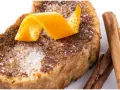 Torrijas al horno espolvoreadas con azúcar y canela, decoradas con piel de naranja y acompañadas de ramas de canela.