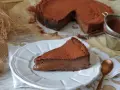 Una porción de tarta de chocolate, cubierta de cacao en polvo, reposa en un plato blanco. El resto de la tarta, también espolvoreada, se ve al fondo.