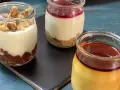 Tres postres en frascos: uno con nueces, otro con mermelada y galleta, y un flan de queso con caramelo.