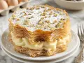 Deliciosa tarta árabe de capas crujientes y crema pastelera, espolvoreada con azúcar glas y nueces picadas.
