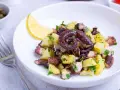 Ensalada de pulpo y patatas, un ejemplo de recetas sanas con pulpo. Servida en plato blanco con limón y perejil.