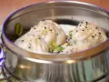 Deliciosos dumplings al vapor, cubiertos con semillas de sésamo y cebolleta, servidos en una vaporera metálica.