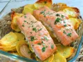 Dos filetes de salmón al horno con patatas crujientes y perejil picado, servidos en una fuente de vidrio.