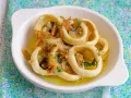 Calamares encebollados en un plato blanco, con cebolla caramelizada y perejil, sobre un mantel azul y verde.