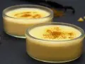 Dos cuencos de natillas caseras, espolvoreadas con canela, junto a palitos de canela y vainilla.
