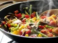 Un delicioso salteado de verduras humeante en un wok, con pimientos, judías verdes, champiñones y cebolla morada.