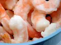 Langostinos cocidos congelados en un bol azul. Aprende cómo descongelar langostinos cocidos fácilmente para tus recetas.