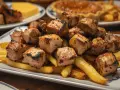 Sabroso raxo gallego a la parrilla, servido sobre patatas fritas crujientes. Un plato contundente y delicioso.