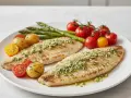 Dos filetes de merluza a la plancha con hierbas, acompañados de patatas pequeñas, espárragos y tomates cherry.