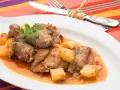 Sabroso cordero al chilindrón con patatas, servido en plato blanco con cubiertos atados con hilo.