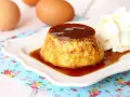 Delicioso flan de huevo casero con caramelo líquido y una porción de nata montada. Huevos frescos al fondo.