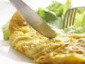 Un cuchillo corta una dorada tortilla francesa servida con hojas de lechuga fresca.