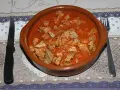 Un cuenco de barro rebosante de magro con tomate, listo para ser disfrutado con pan y vino tinto.