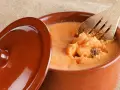 Un cuenco de barro con lomo en manteca, listo para ser servido. Una cuchara de madera remueve la deliciosa preparación.