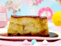 Un trozo de pan de calatrava, con su caramelo dorado, reposa en un plato blanco. Al fondo, una taza rosa y un limón.