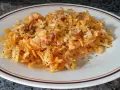 Bacalao dorado desmenuzado con patatas fritas finas y perejil picado, servido en un plato blanco con borde marrón y naranja.