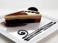 Deliciosa tarta de tres chocolates, con capas de mousse de chocolate blanco, con leche y negro, decorada con cacao y un toque de galleta.