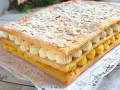 Delicioso pastel de milhojas de crema, con capas de hojaldre crujiente, crema pastelera amarilla y crema batida blanca, espolvoreado con azúcar glas y almendras laminadas.