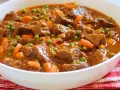 Ternera a la jardinera en un cuenco blanco, con trozos de carne tierna, zanahorias y guisantes en una salsa sabrosa.