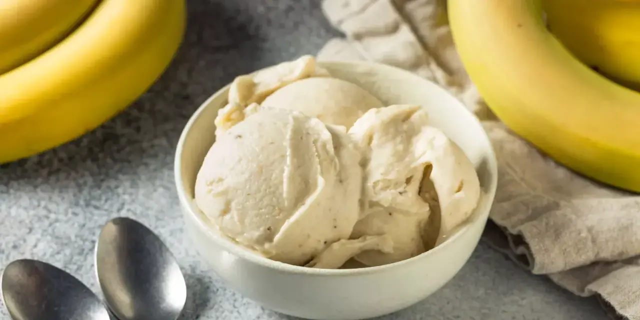 Delicioso helado de plátano cremoso en un tazón blanco, con plátanos amarillos frescos al lado.