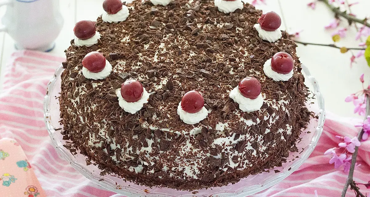Deliciosa tarta Selva Negra, cubierta de virutas de chocolate y coronada con cerezas y nata.