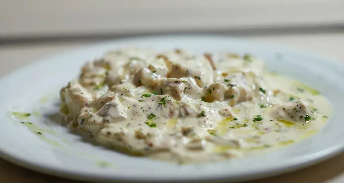 Deliciosa brandada de bacalao cremosa, con trozos de pescado blanco y perejil picado, servida en un plato blanco.