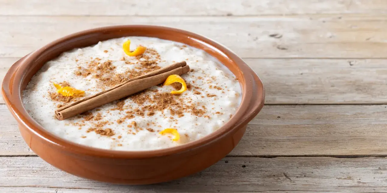 Un tazón de arroz con leche cremoso, espolvoreado con canela y adornado con cáscara de naranja y una rama de canela.