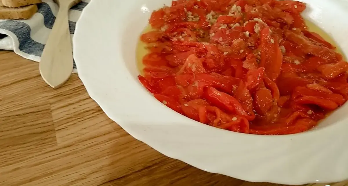 Asadillo manchego, pimientos asados con ajo y aceite, listos para disfrutar con tostadas y una cuchara de madera.