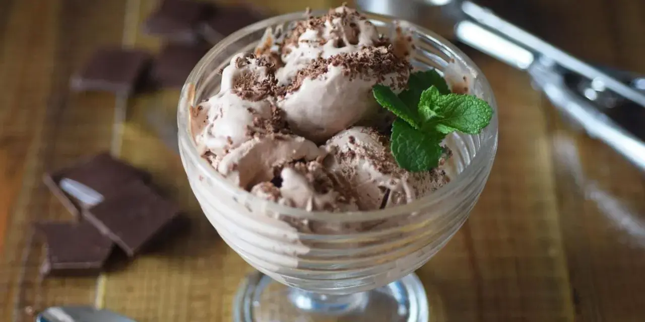 Delicioso helado de chocolate con virutas de chocolate y una hoja de menta, servido en copa de cristal.