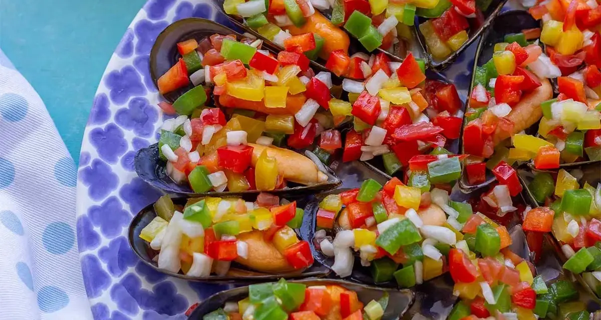 Mejillones a la vinagreta, cubiertos con una colorida mezcla de pimientos picados y cebolla.