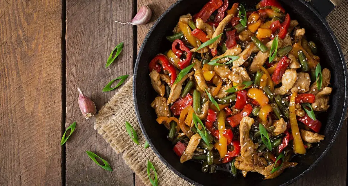 Sabroso wok de pollo con pimientos de colores y judías verdes, espolvoreado con semillas de sésamo y cebolleta.