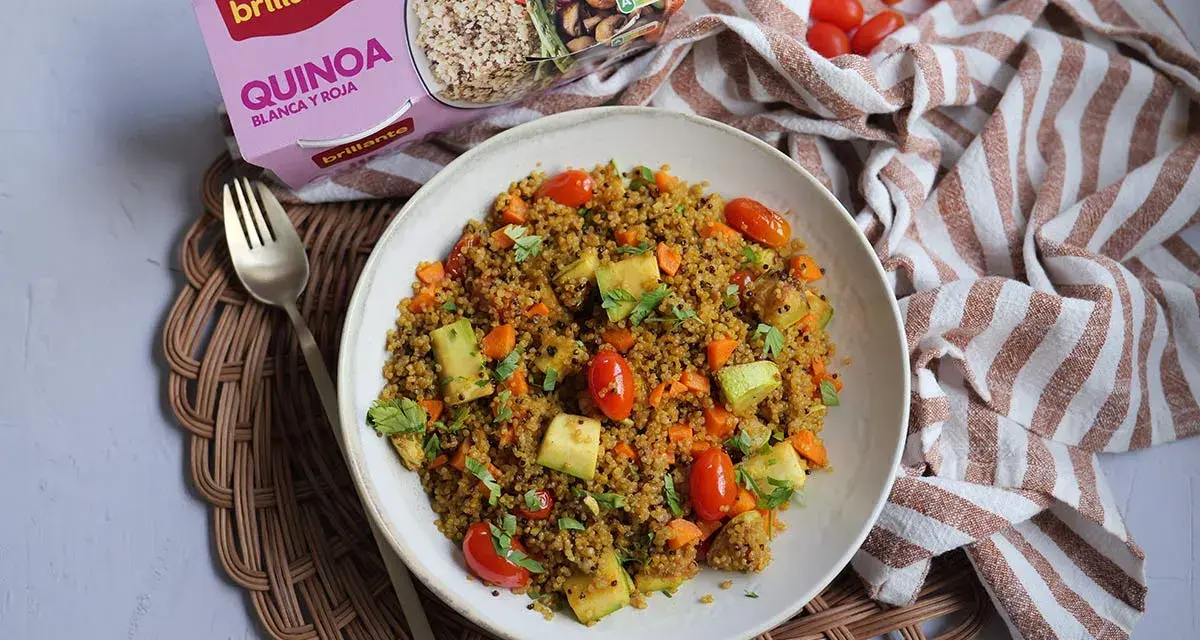 Un plato de quinoa con verduras, incluyendo tomates cherry, calabacín y zanahoria, listo para disfrutar.