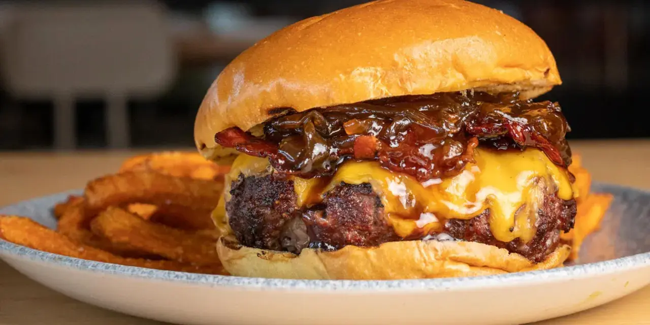 La mejor receta de hamburguesas caseras: jugosa carne, queso fundido, cebolla caramelizada y crujientes patatas fritas.