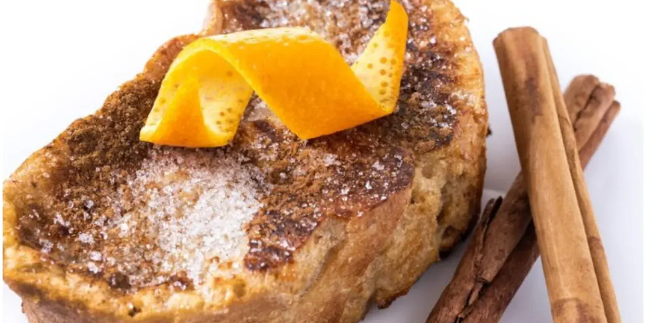 Torrijas al horno espolvoreadas con azúcar y canela, decoradas con piel de naranja y acompañadas de ramas de canela.