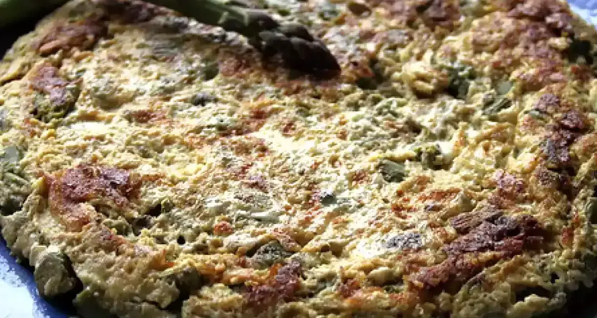 Tortilla de esparragos dorada y esponjosa, con espárragos frescos encima, servida en un plato azul.