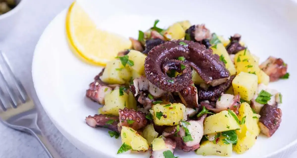 Ensalada de pulpo y patatas, un ejemplo de recetas sanas con pulpo. Servida en plato blanco con limón y perejil.