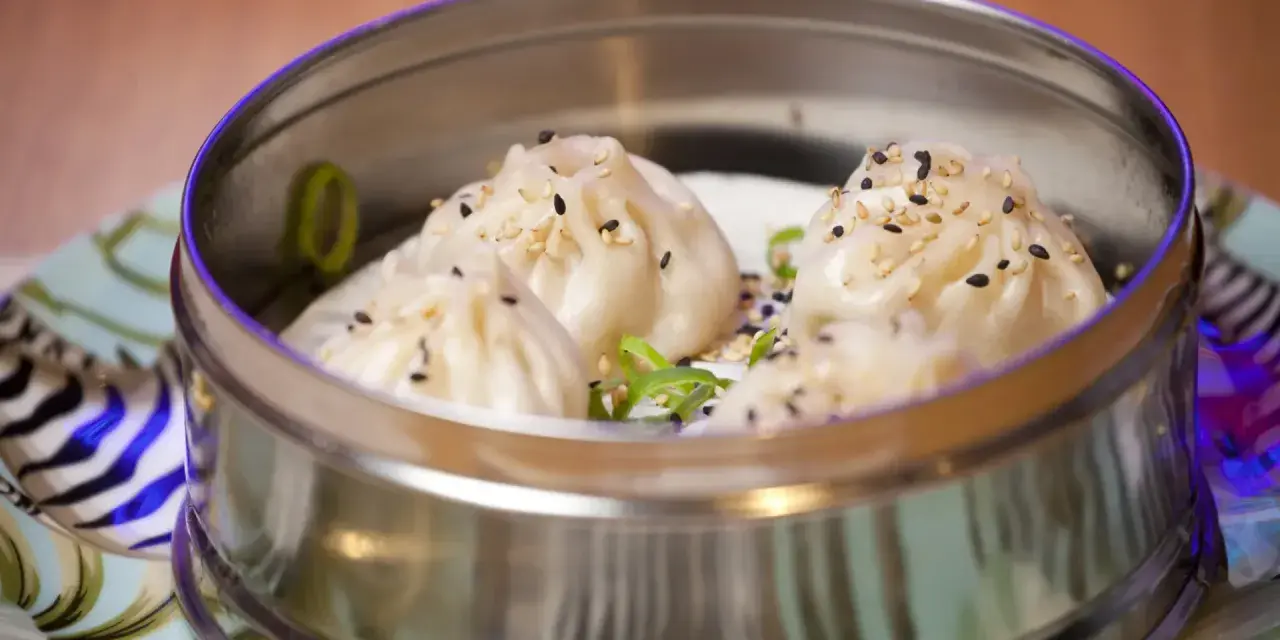 Deliciosos dumplings al vapor, cubiertos con semillas de sésamo y cebolleta, servidos en una vaporera metálica.
