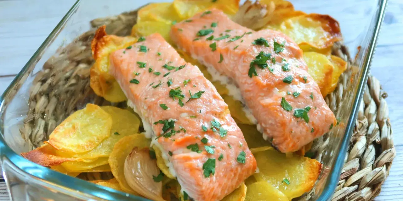 Dos filetes de salmón al horno con patatas crujientes y perejil picado, servidos en una fuente de vidrio.