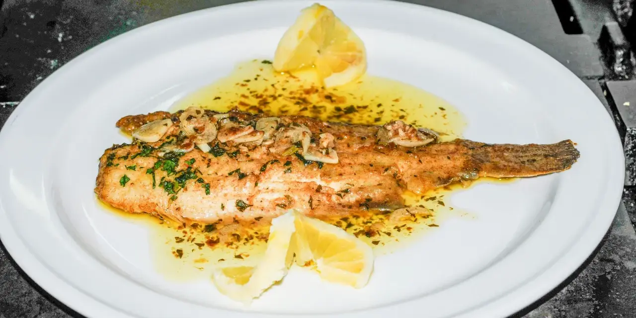 Delicioso lenguado a la meunière, bañado en mantequilla dorada, ajo y perejil, con gajos de limón.