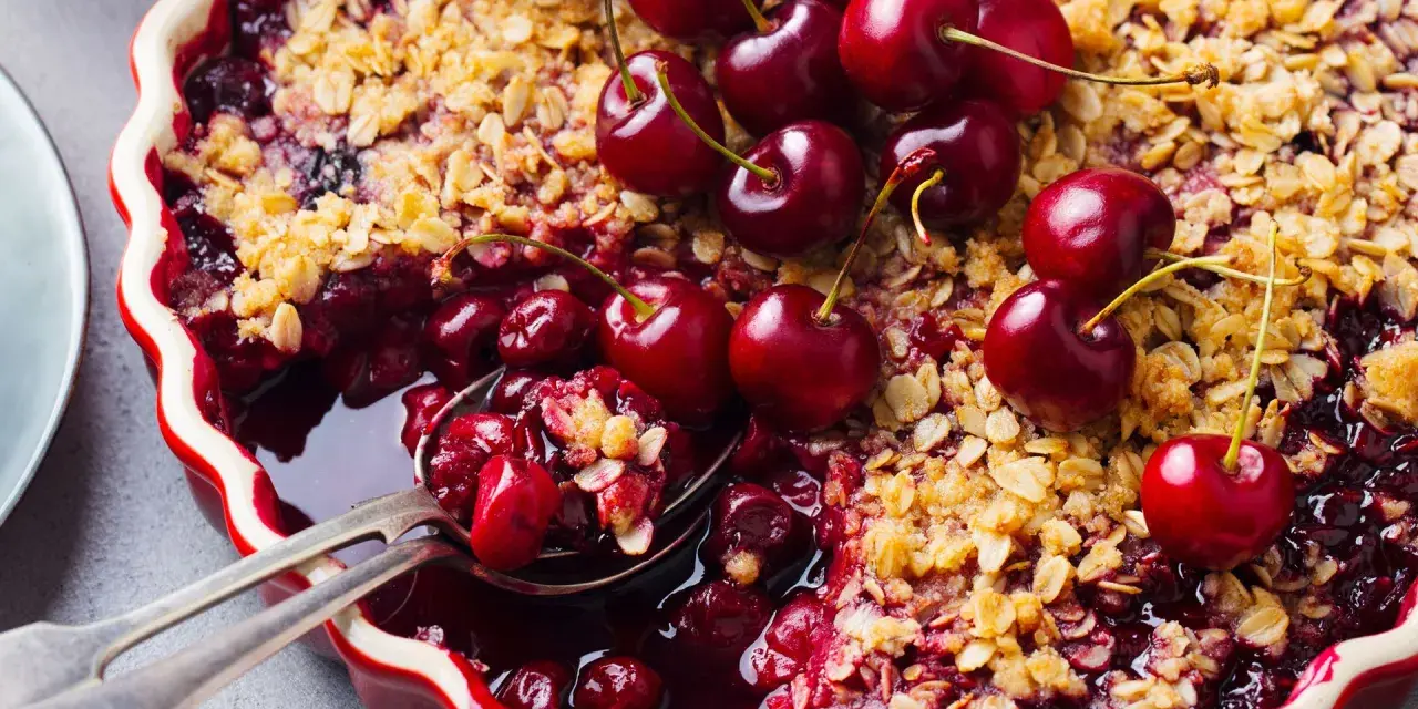 Delicioso postre con cerezas, cubierto de crumble dorado y adornado con cerezas frescas.