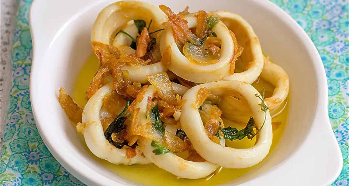 Calamares encebollados en un plato blanco, con cebolla caramelizada y perejil, sobre un mantel azul y verde.