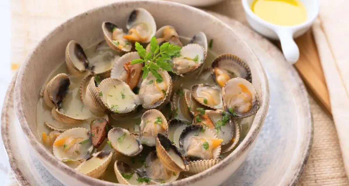 Deliciosos tipos de berberechos cocinados en su jugo, servidos en un cuenco de cerámica con perejil picado.