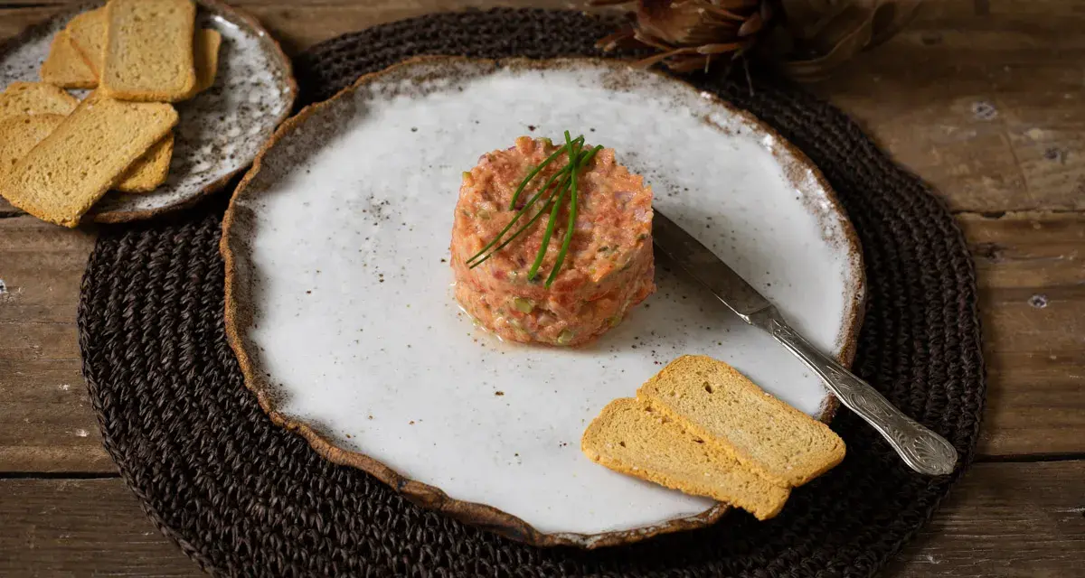 Delicioso tartar de tomate, servido con tostas crujientes y un cuchillo de plata. Un plato fresco y vibrante.